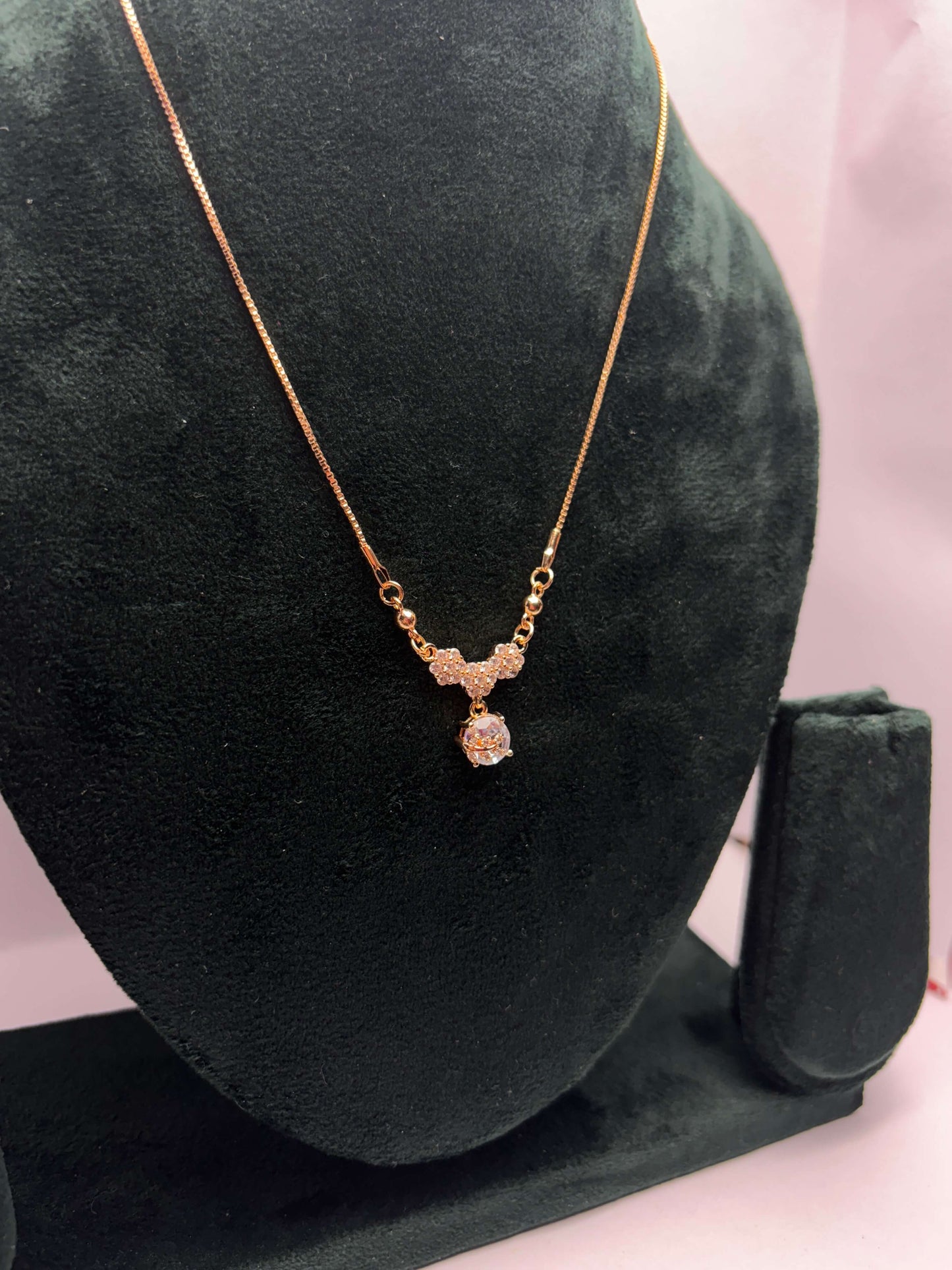 Gold necklace with a pendant on a green velvet stand.