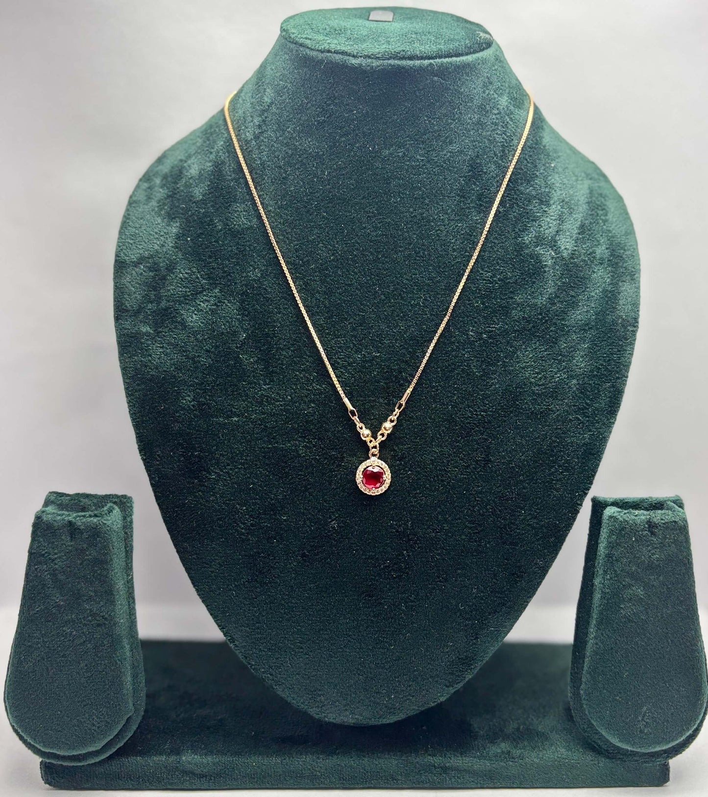 Gold necklace with a red gemstone pendant .
