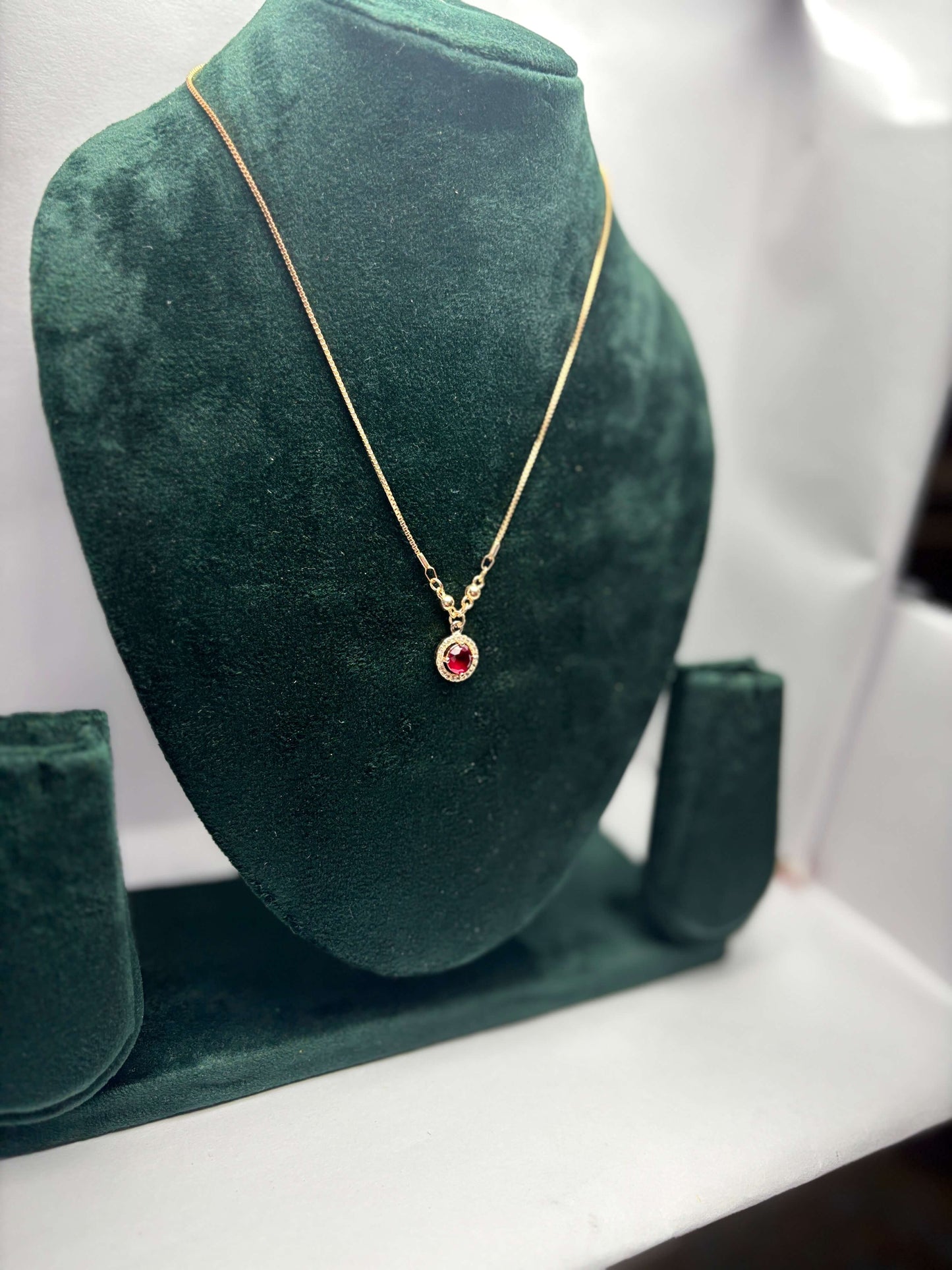 Gold necklace with a red gemstone pendant.