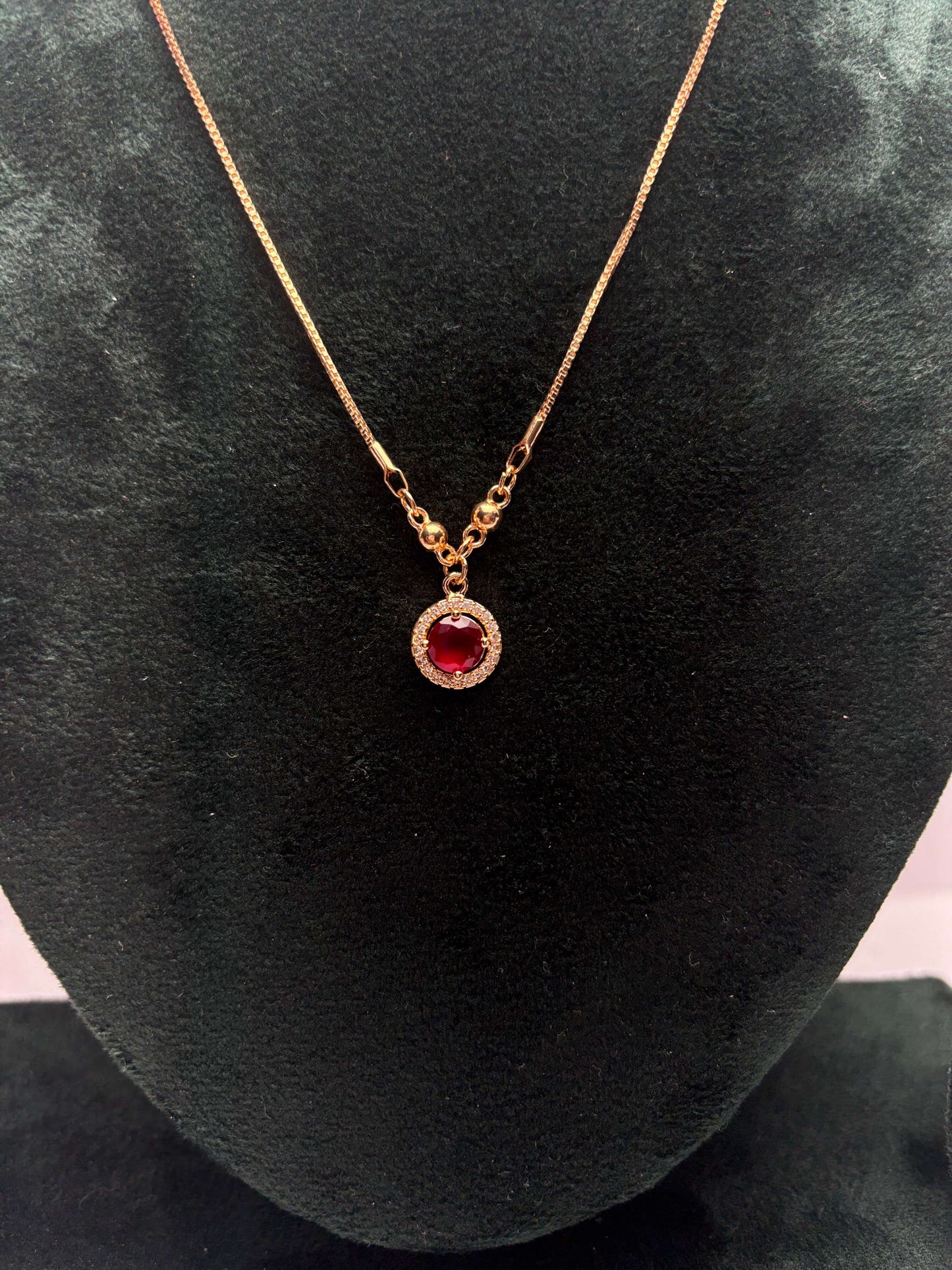 Gold necklace with a red gemstone pendant.