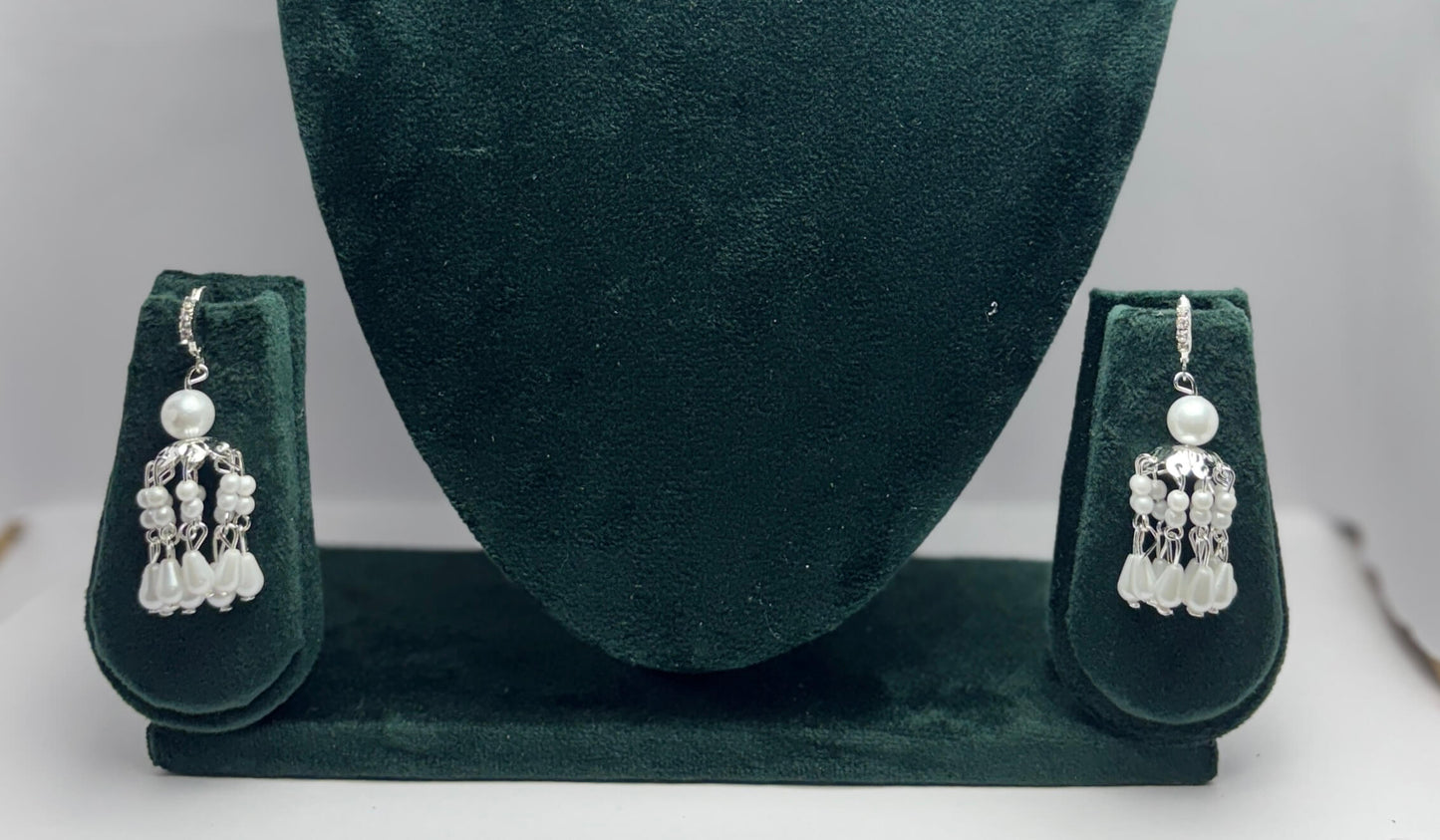 Pair of silver earrings with pearls on a green velvet stand.