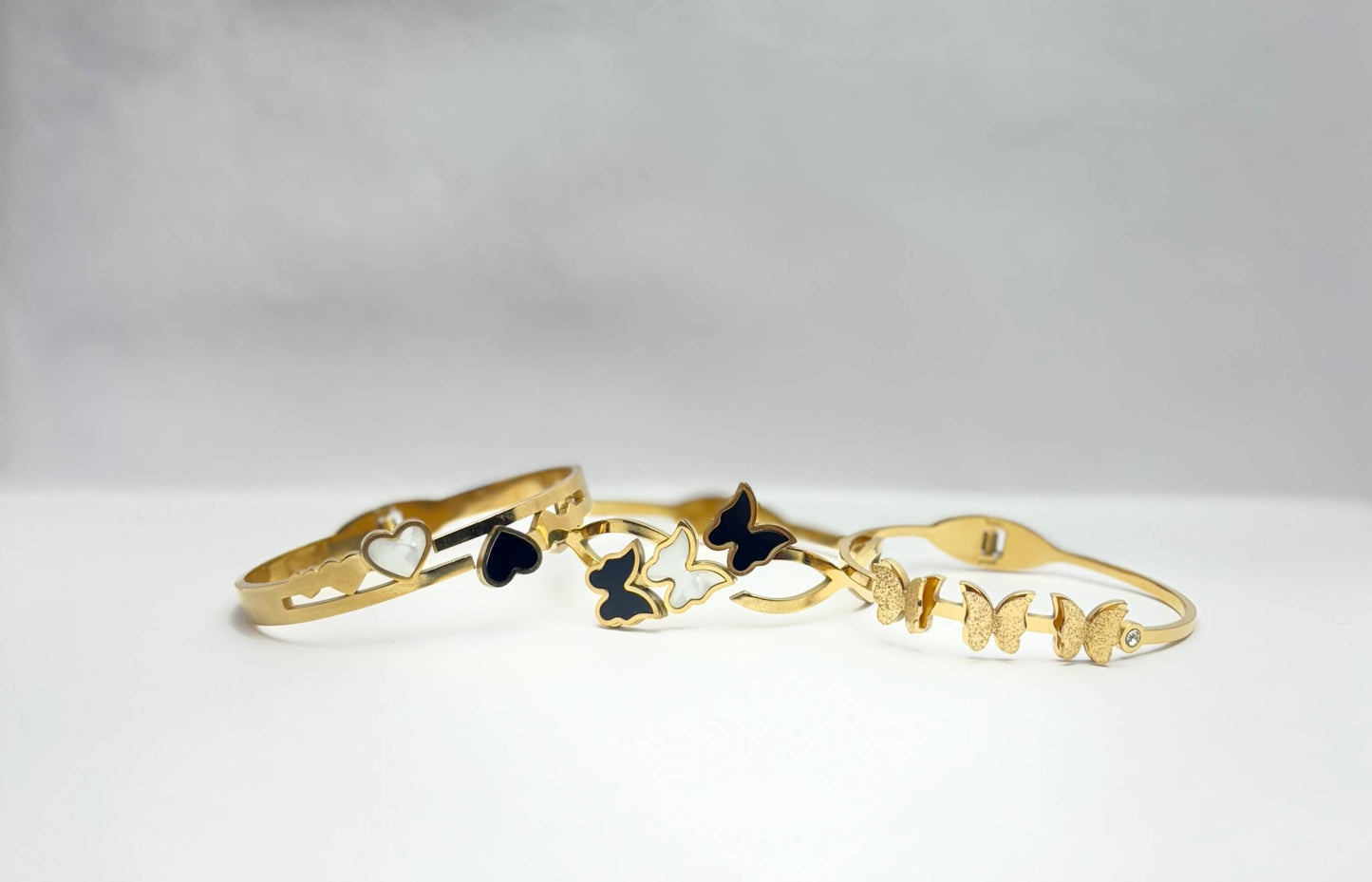 Gold bracelet with butterfly and heart charms on a white background