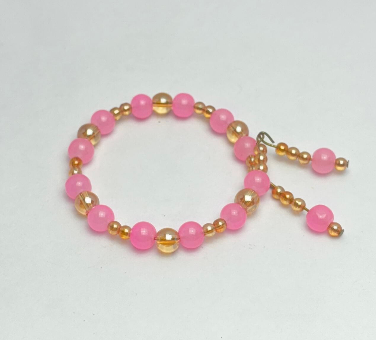 Beaded bracelet with pink and gold beads on a light gray background