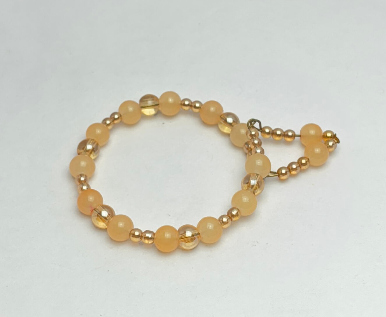 Beaded bracelet with gold and beige beads on a light gray background