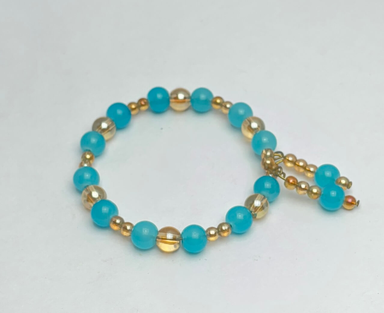 Bracelet with turquoise beads and gold accents on a light gray background