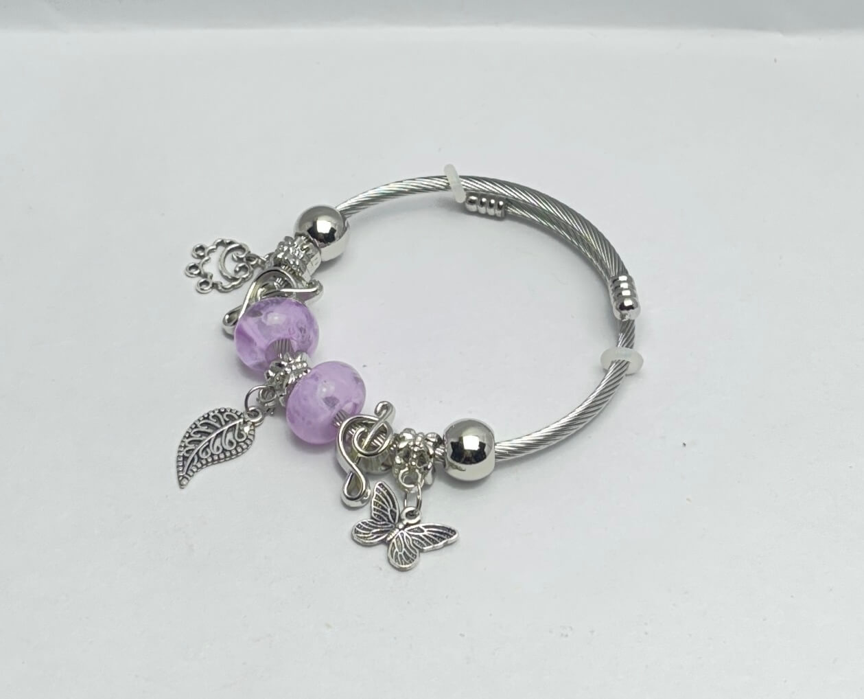 Silver bracelet with purple beads and charms on a white background