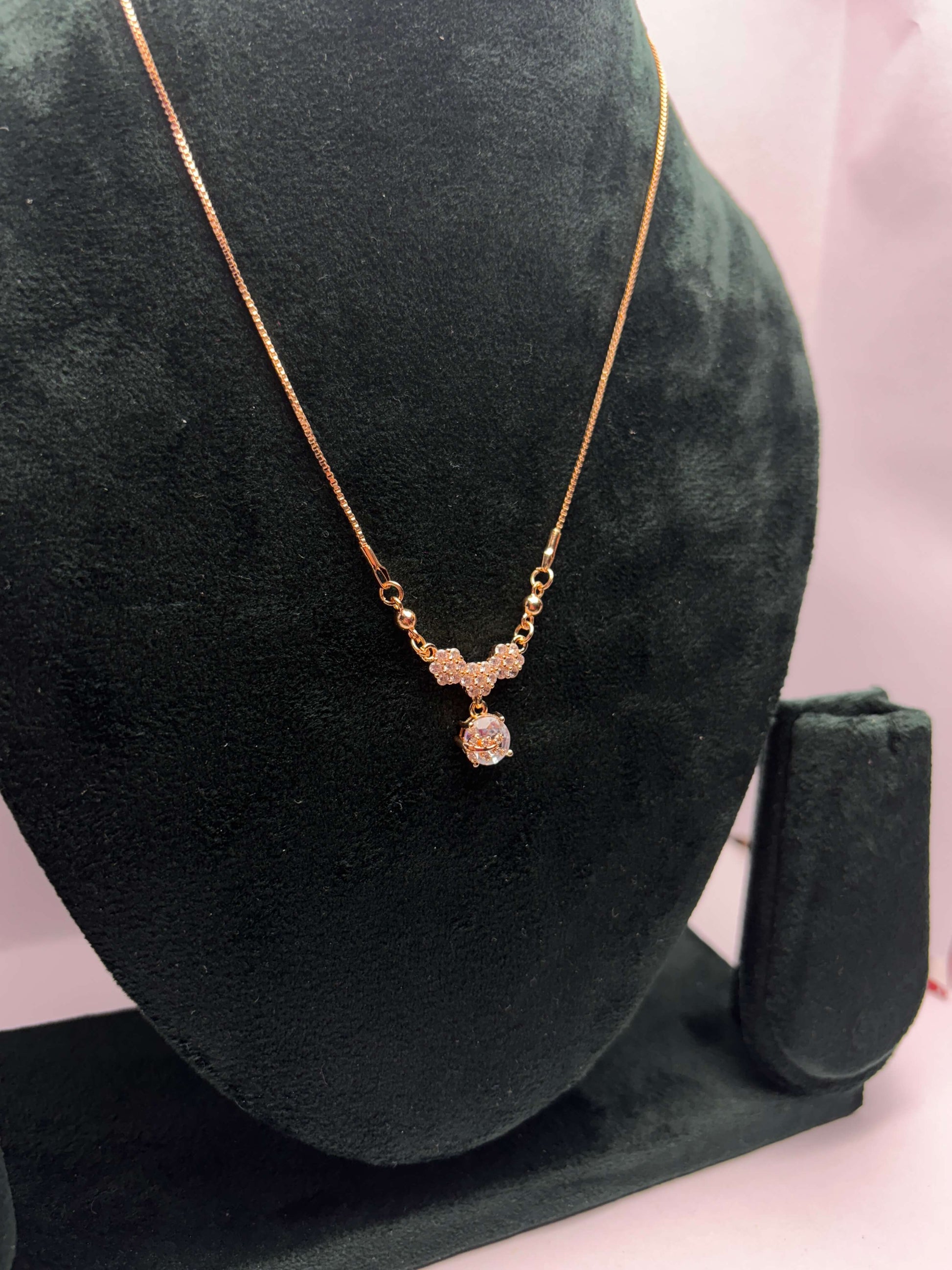 Gold necklace with a pendant on a green velvet stand.