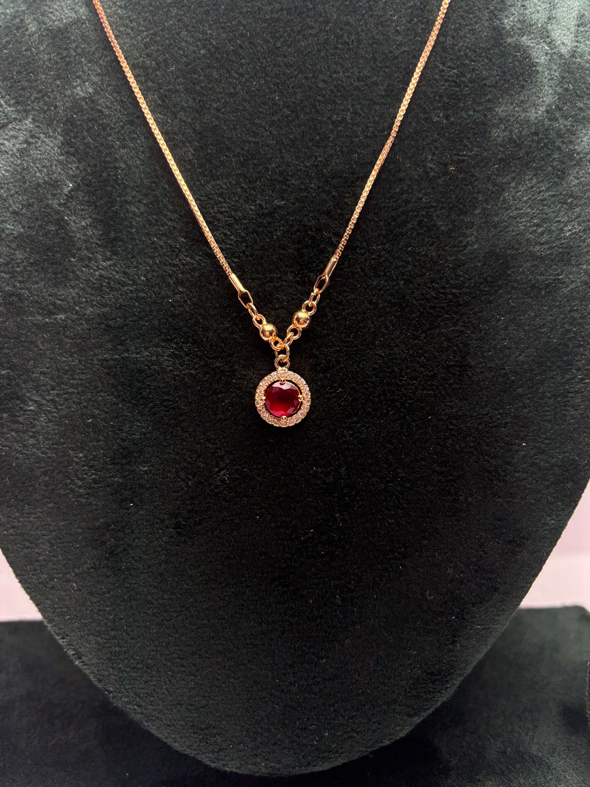 Gold necklace with a red gemstone pendant.