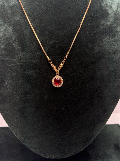 Gold necklace with a red gemstone pendant.