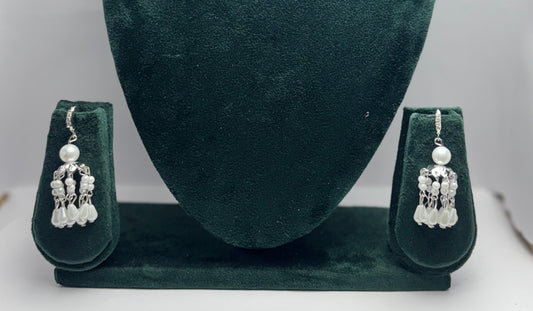 Pair of silver earrings with pearls on a green velvet stand.
