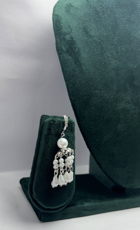 Pearl earring on a green velvet stand with a gray background
