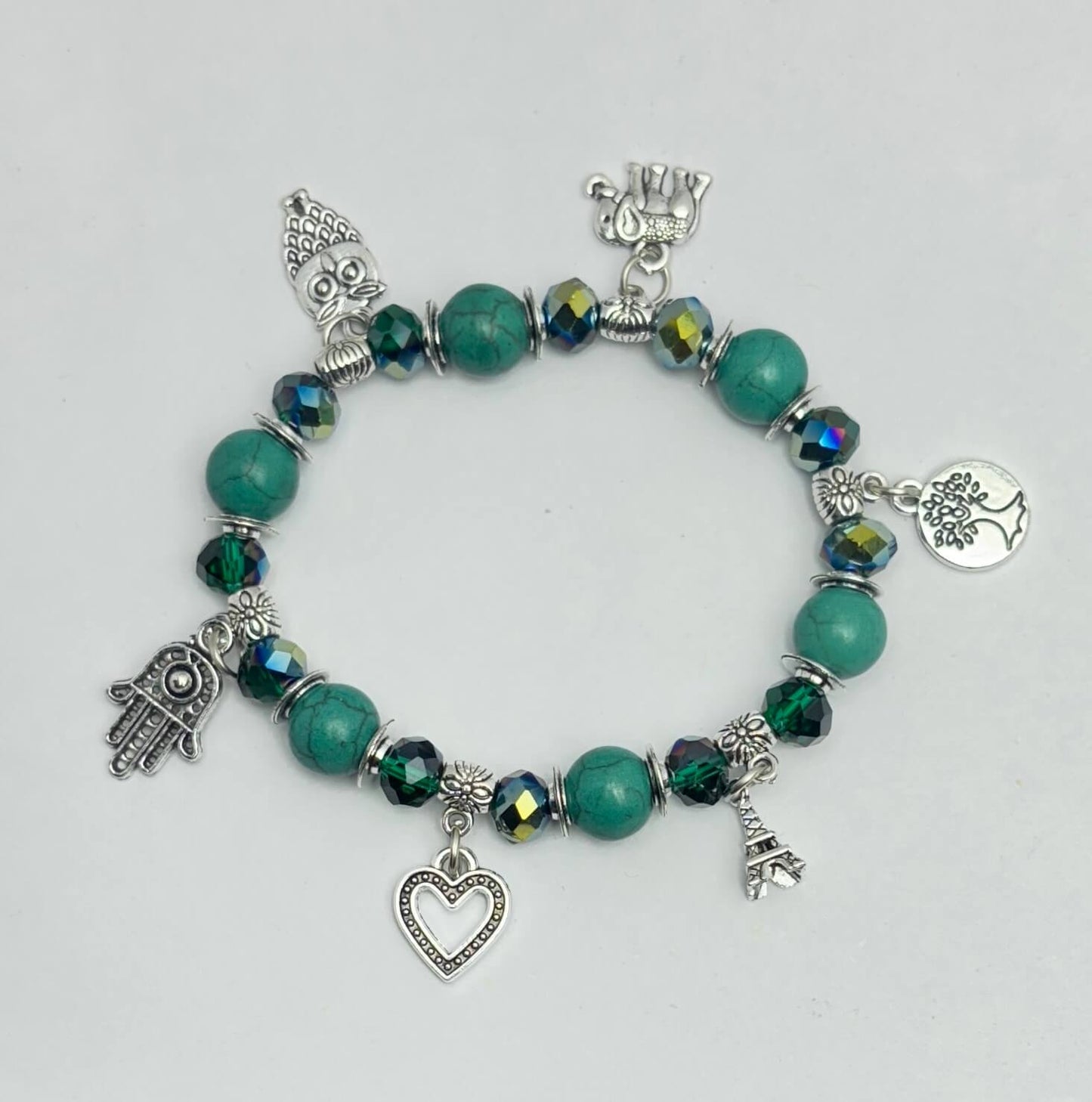 Bracelet with green beads and various charms on a light gray background