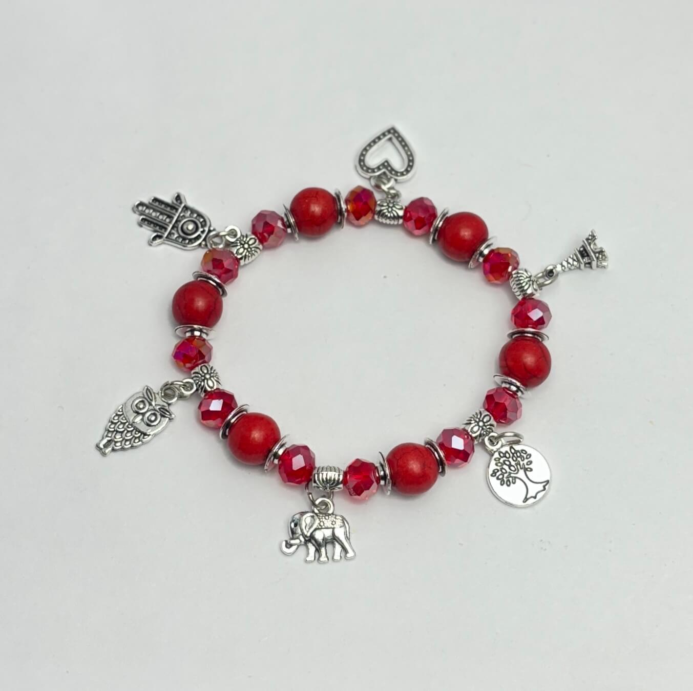 Bracelet with red beads and various silver charms on a light gray background